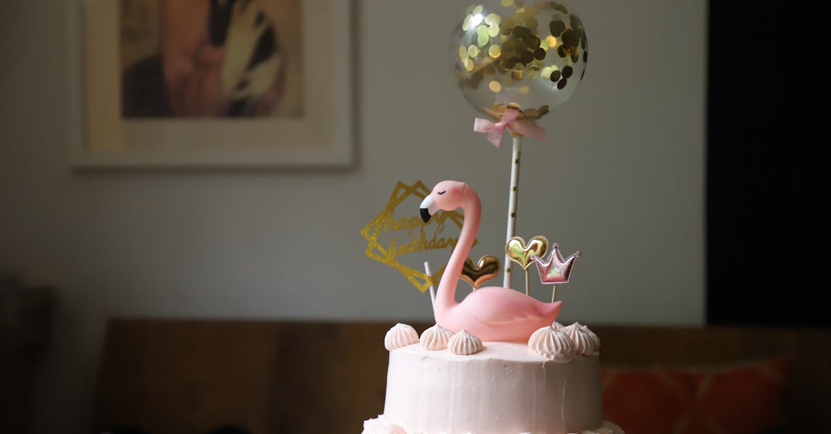 Elegant pink birthday cake with flamingo and balloon decorations indoors.