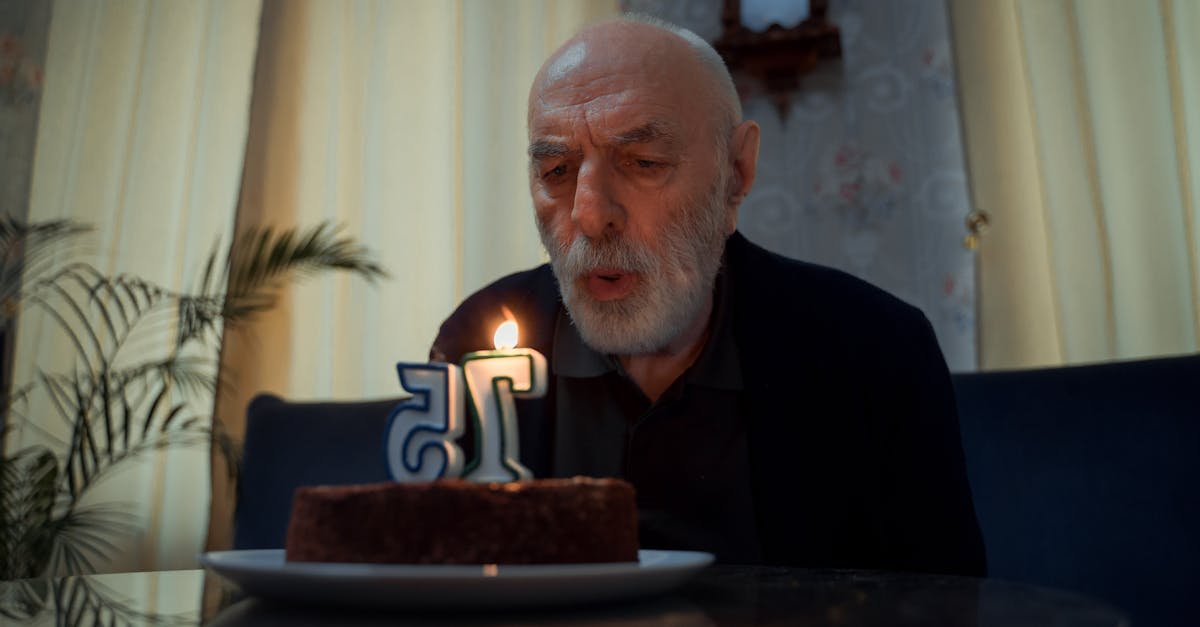 Senior man blowing candle on a 75th birthday cake indoors.