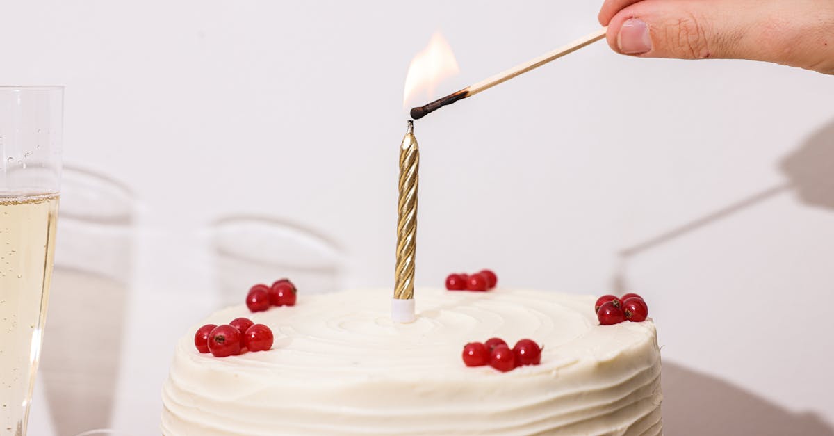 A hand lighting a candle on a white frosted berry-decorated cake, ideal for celebrations.