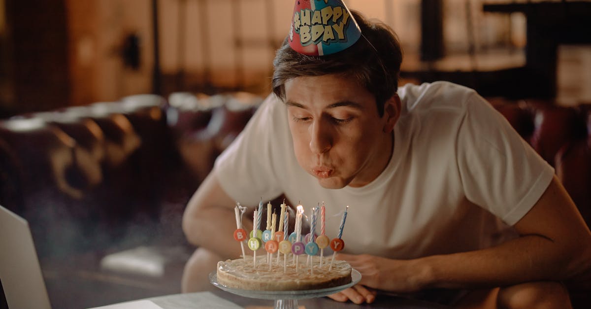 A young man celebrates his birthday with a cake and a laptop in a cozy home setting.