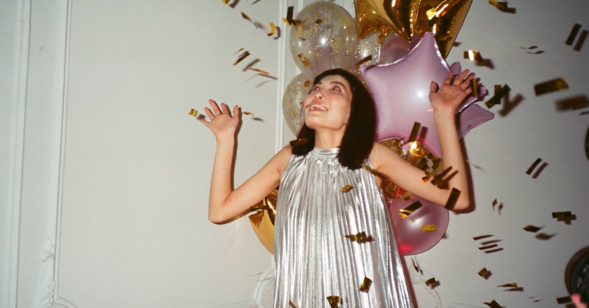 A woman in a silver dress celebrates with balloons and confetti indoors.