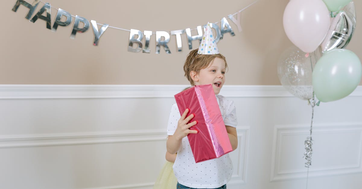 A young boy celebrates his birthday indoors with balloons and a present in hand.