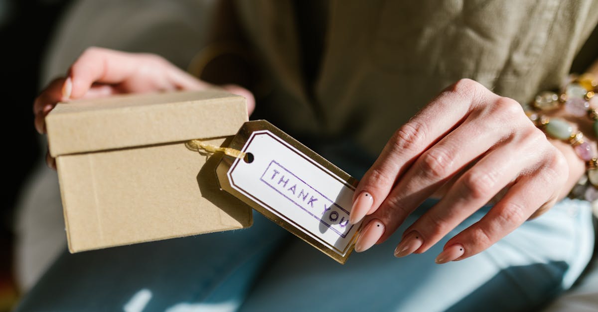 Close-up of hands holding a gift box with a Thank You tag attached, in natural lighting.