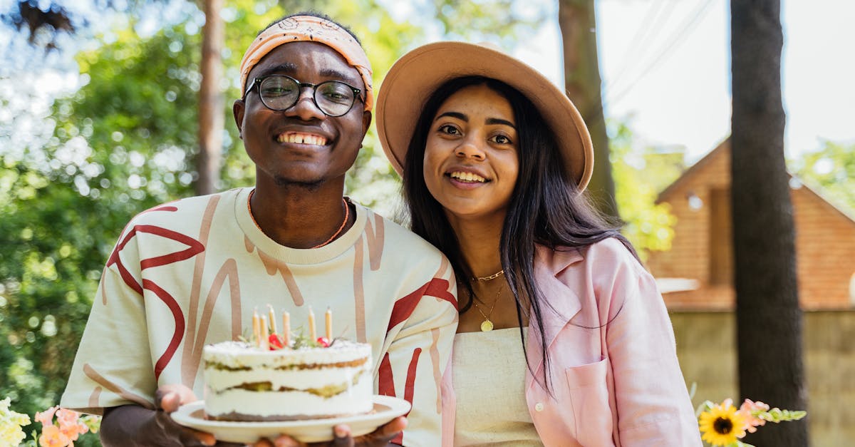 Two adults celebrating a birthday outdoors with a cake adorned with candles, smiling and happy.