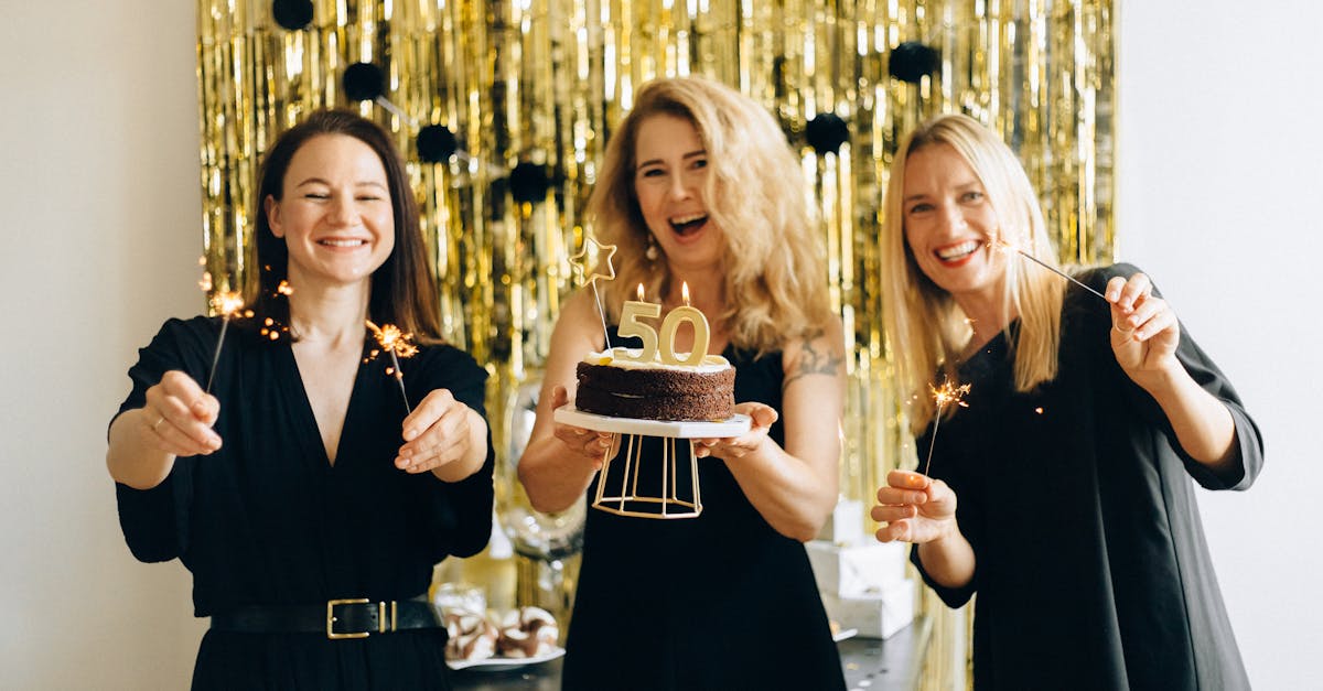 Happy women celebrating a 50th birthday with cake and sparklers indoors.