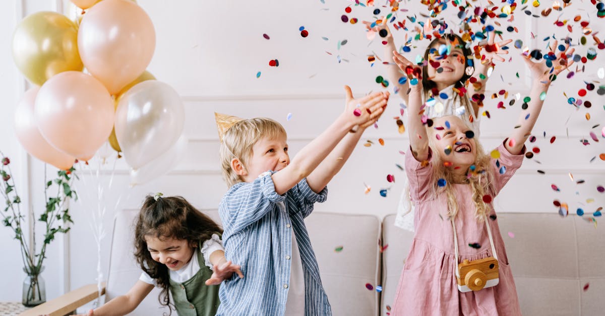 A group of children celebrating a birthday party with colorful balloons and confetti indoors.