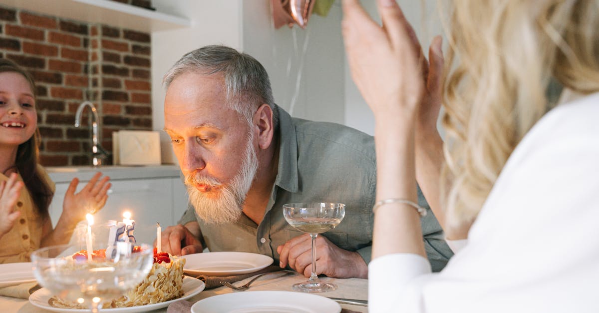 A senior man celebrates his birthday by blowing out candles on a cake in a cozy indoor setting.