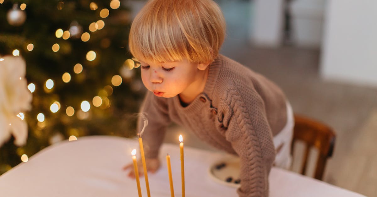 Young child blowing out candles on a birthday cake indoors, festive atmosphere.