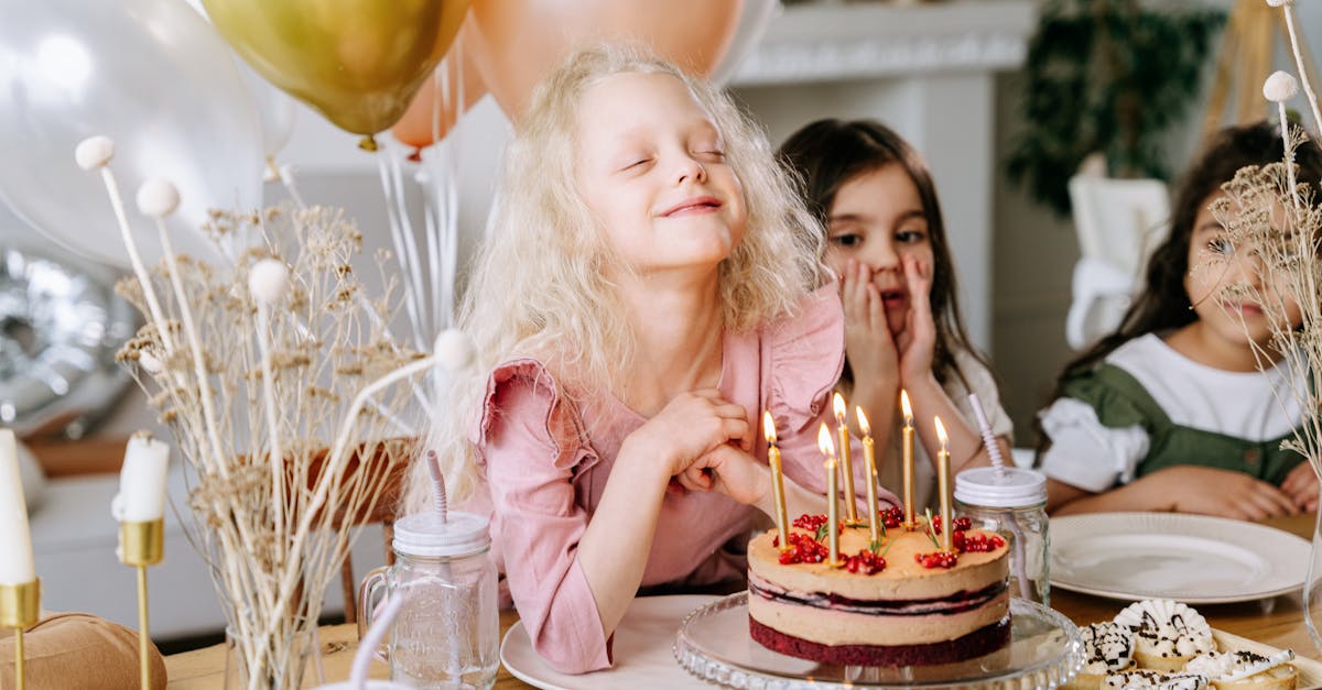 A happy girl makes a wish with lighted candles on her birthday cake, surrounded by friends and balloons.