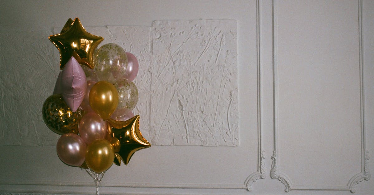 Gold and pink balloons forming a decorative bouquet against a textured white wall.